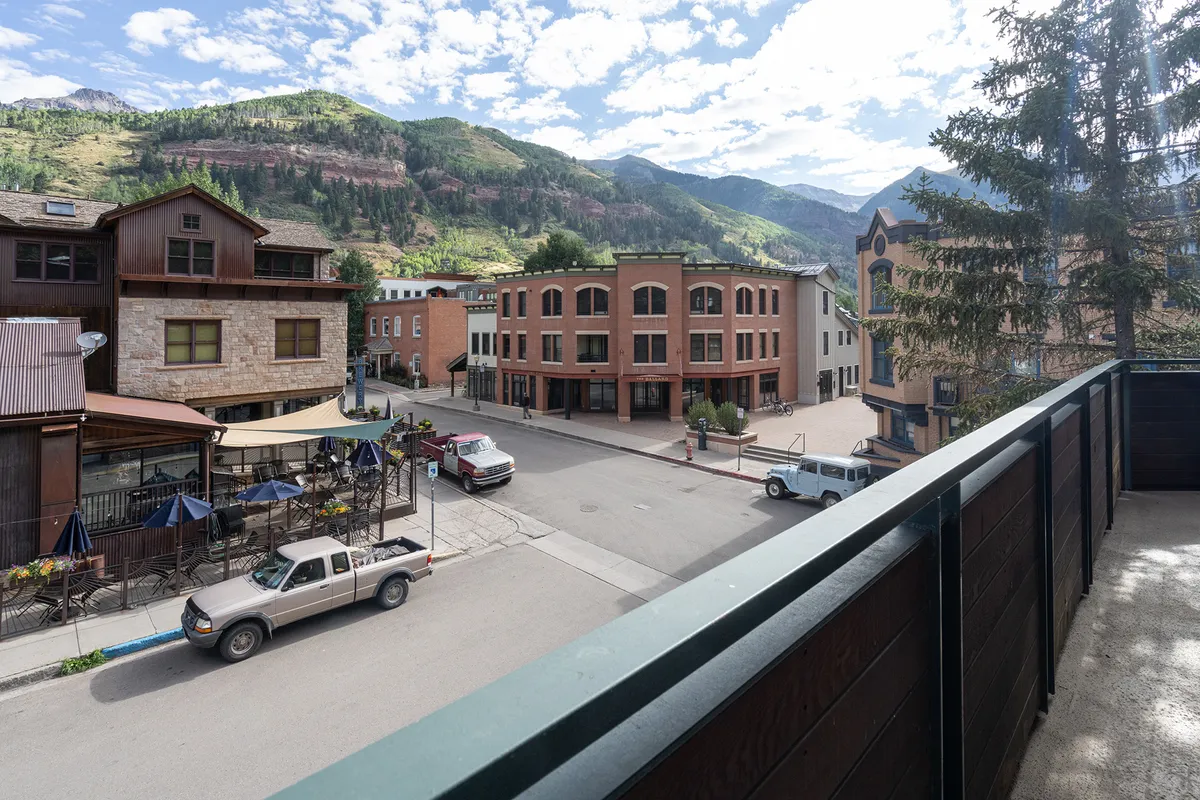 A bustling town square framed by historic architecture and mountain views, with people walking, shopping, and dining outdoors. The lively atmosphere hints at local festivals, family-friendly dining, and easy access to community life.