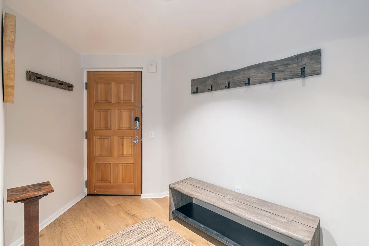 This inviting entryway scene features a sturdy wooden door, a comfortable bench, and a hat rack. The atmosphere is warm and welcoming, suggesting thoughtful design and a sense of arrival for residents and guests alike.