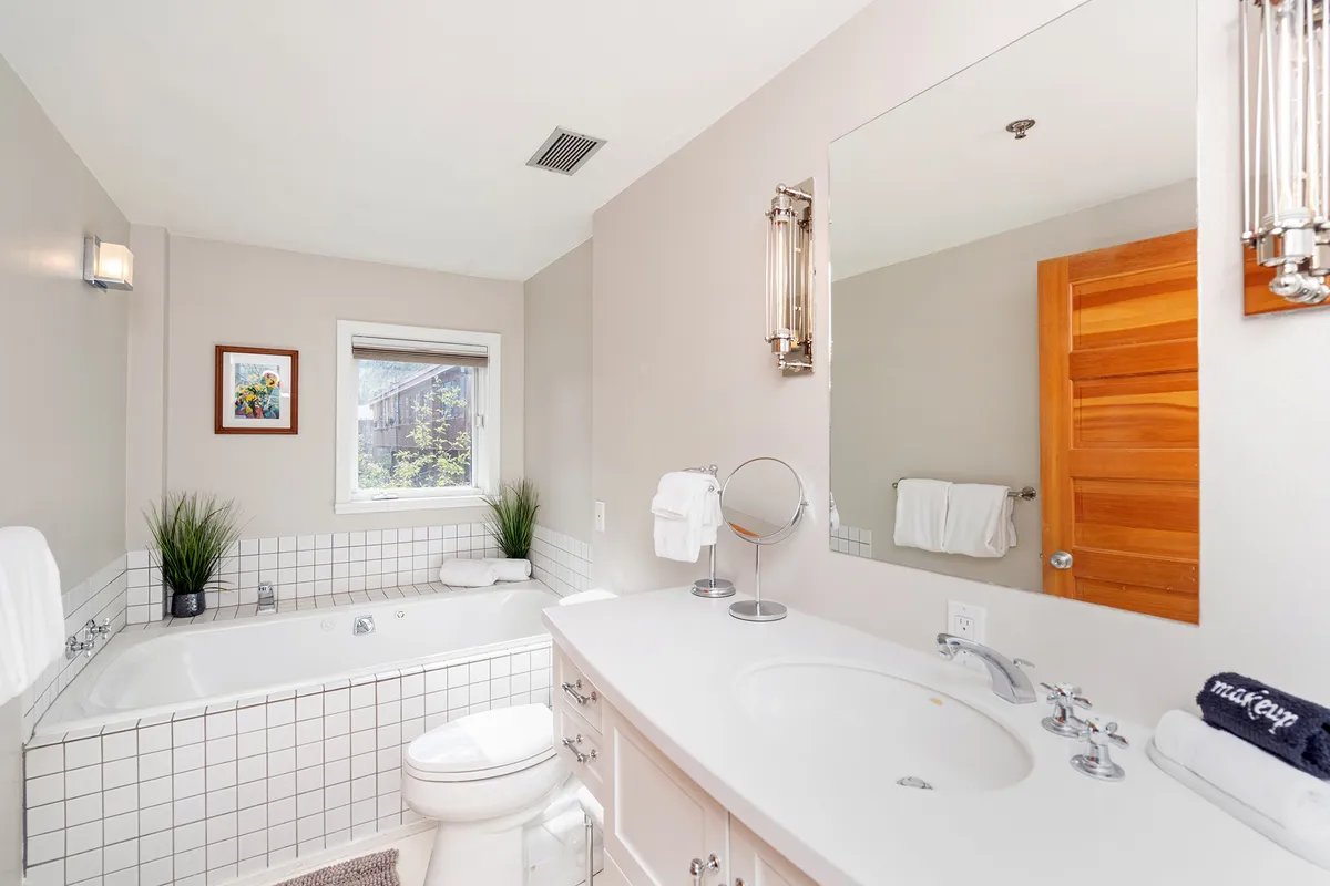 A tranquil bathroom scene with a soaking bathtub, sink, window letting in natural light, and tasteful artwork. The space invites relaxation and self-care, ideal after a day outdoors.