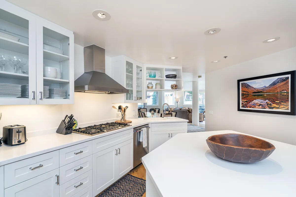 A functional kitchen scene emphasizing a kitchen island with a bowl, a visible gas stove, framed artwork, and shelves adorned with glassware. The welcoming space suggests both daily use and special gatherings, blending practicality with warmth.
