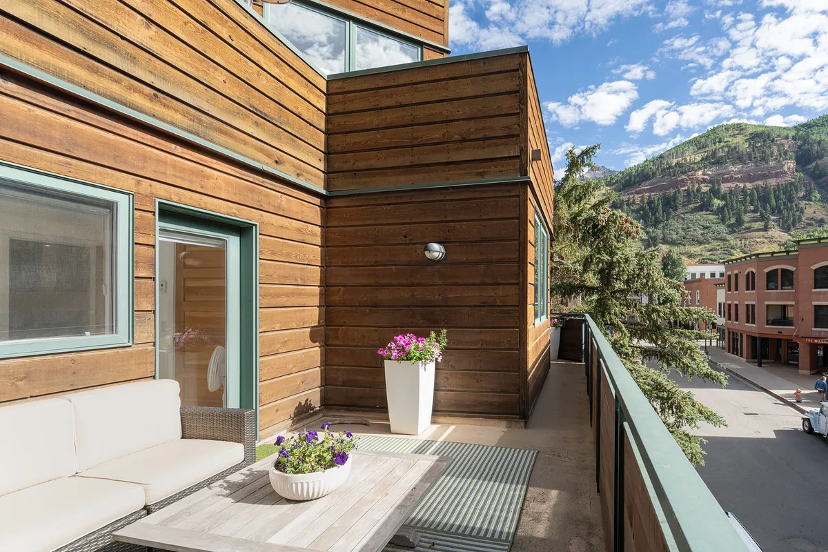 This image presents a peaceful balcony space with wooden siding, comfortable outdoor furniture, and colorful flower pots. The setting is perfect for morning coffee or evening relaxation, surrounded by scenic beauty and the fresh mountain air.