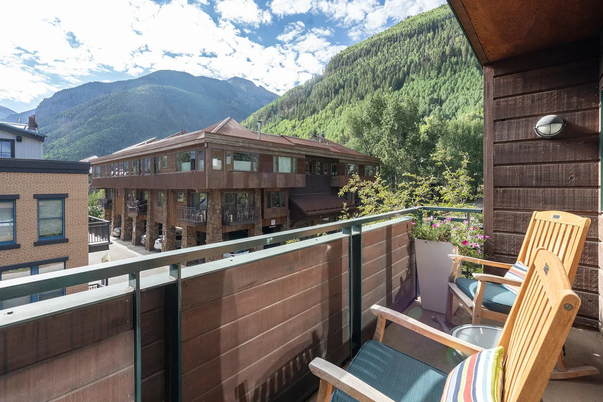 This image presents a tranquil scene from a balcony or terrace, featuring comfortable seating and sweeping views of the surrounding mountain range and part of the local architecture. The setting is perfect for relaxing with a drink, enjoying the sunrise, or socializing against a dramatic Telluride backdrop.