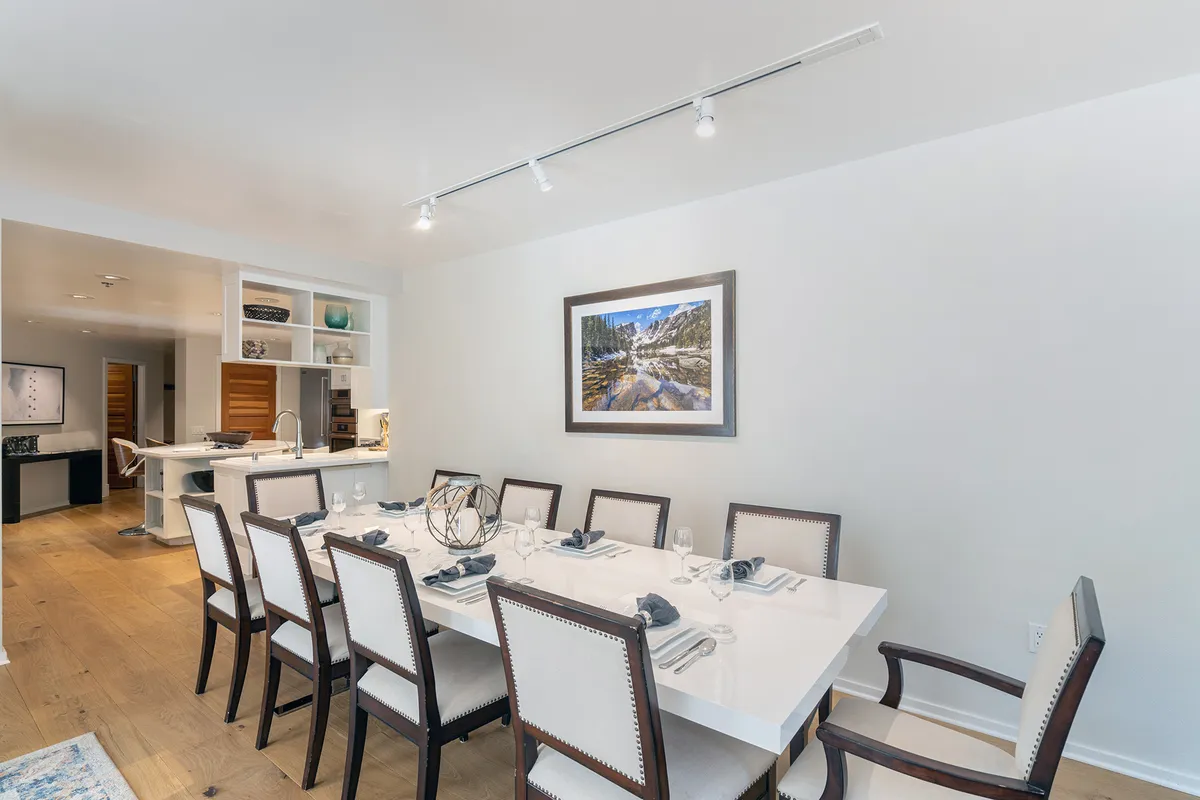 An elegant, well-lit dining space with a large table set for gatherings. Decorative art and stylish lighting create a welcoming atmosphere for shared meals, celebrations, or game nights with friends or another couple.