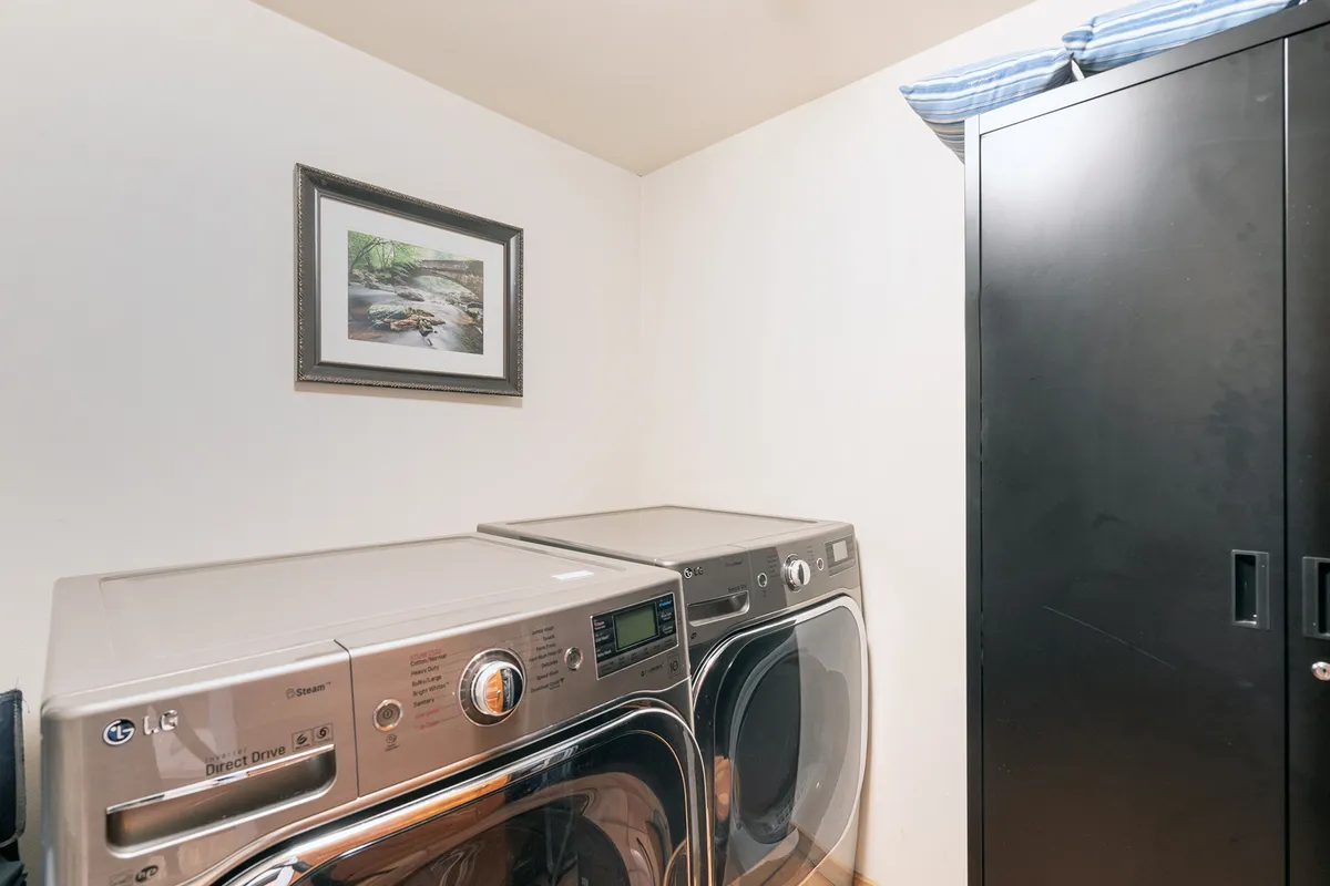 A practical and well-lit laundry room featuring a washer, dryer, framed picture, and black cabinet. The organized setup ensures guests have everything they need for longer stays.