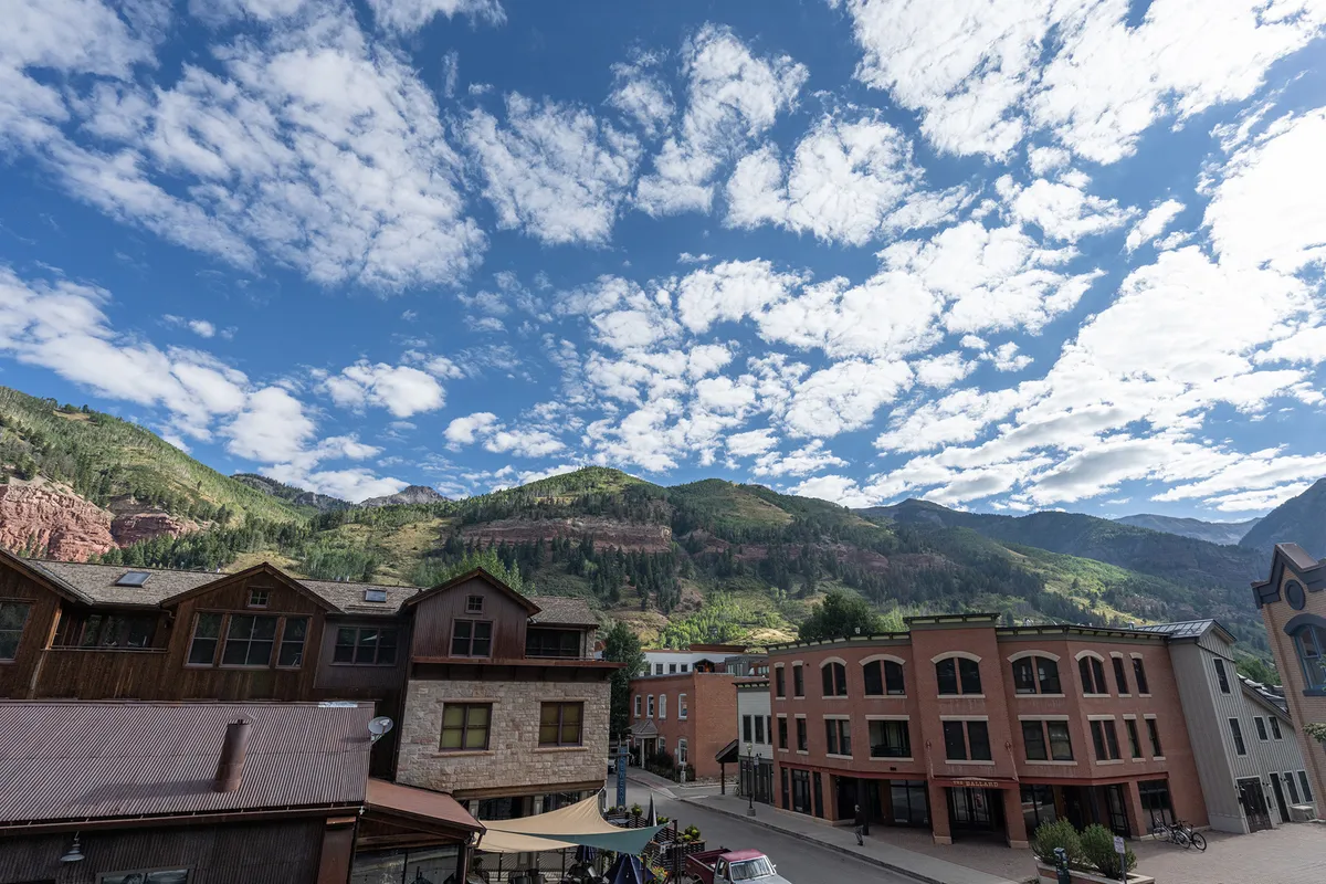 A scenic view captures Telluride’s charming town set against a backdrop of impressive mountains. The image includes buildings and a street scene, evoking a sense of place and community, as well as the vibrancy of downtown living.